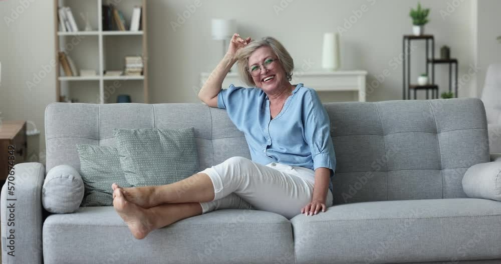 Overjoyed mature woman relaxing on cozy sofa in warm living room laughing smile staring at camera looks carefree feels happy to spend leisure at own modern flat, having untroubled life on retirement Overjoyed mature woman relaxing on cozy sofa in warm living room laughing smile staring at camera looks carefree feels happy to spend leisure at own modern flat, having untroubled life on retirement