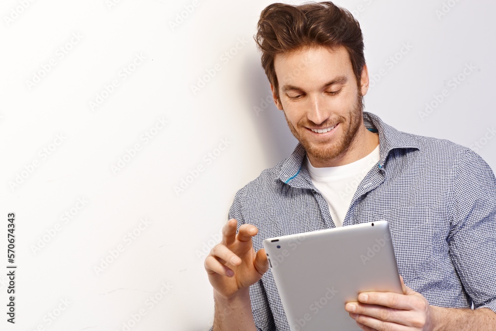 Happy white man working using tablet computer leaning against white wall. Copy space, casual clothing. Happy white man working using tablet computer leaning against white wall. Copy space, casual clothing.