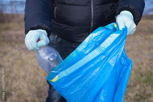 Detail of a volunteer's hand picking up plastic bottle from the forest and putting in the plastic bag. Concept of Earth Day and World Environment Day June 5.