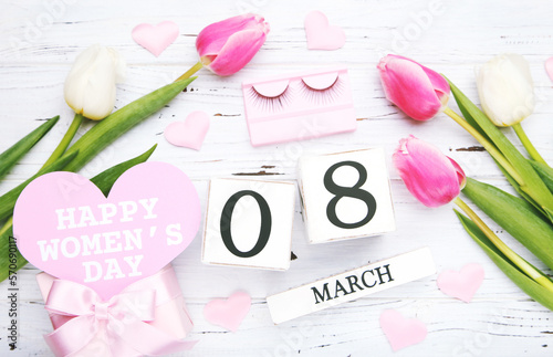 Flowers of tulips and cube calendar, gift box and card in shape of heart with text Happy Women's Day on white wooden background