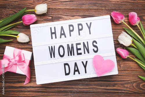 Flowers of tulips and lightbox with text Happy Women's Day, gift box and felt heart on brown wooden background