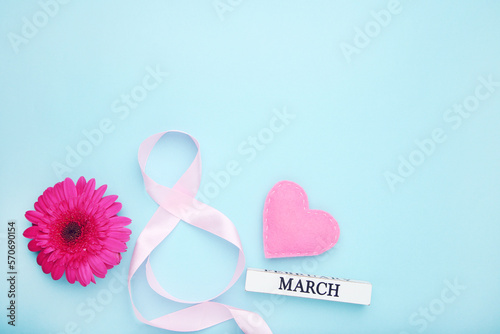 Pink gerbera flower, felt heart and ribbon in shape of figure number 8 on blue background
