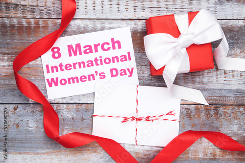 Card with text 8 March International Women's Day, envelope with letter, gift and red ribbon on wooden background