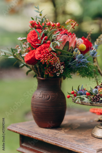 clay jug with flowers on a wooden table. a bouquet of red wild flowers