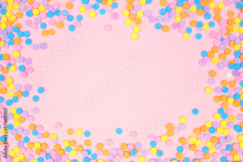 Colorful candy sprinkles frame. Top view on a pink background. Pastel color theme. Copy space.