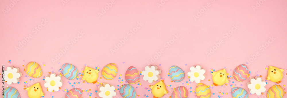 Easter candy bottom border. Colorful pastel candy eggs, chicks and flowers. Top down view against a pink banner background. Copy space.