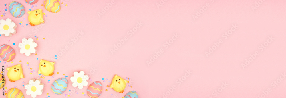 Easter candy corner border. Colorful pastel candy eggs, chicks and flowers. Above view against a pink banner background. Copy space.