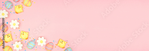 Easter candy corner border. Colorful pastel candy eggs, chicks and flowers. Above view against a pink banner background. Copy space.