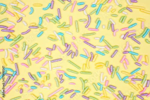 Colorful candy sprinkles background. Above view on a yellow background. Pastel Easter color theme.