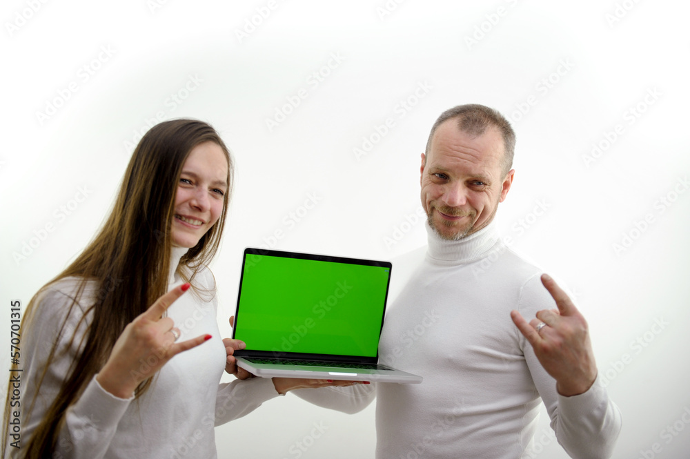 man and girl stand on white background in hands of laptop with green blank screen show gesture with little finger and forefinger goat magical sign protects from evil place for advertising satisfied man and girl stand on white background in hands of laptop with green blank screen show gesture with little finger and forefinger goat magical sign protects from evil place for advertising satisfied
