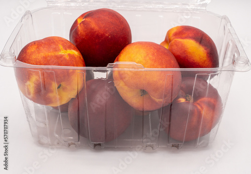 Nectarines in a plastic container on a white background.