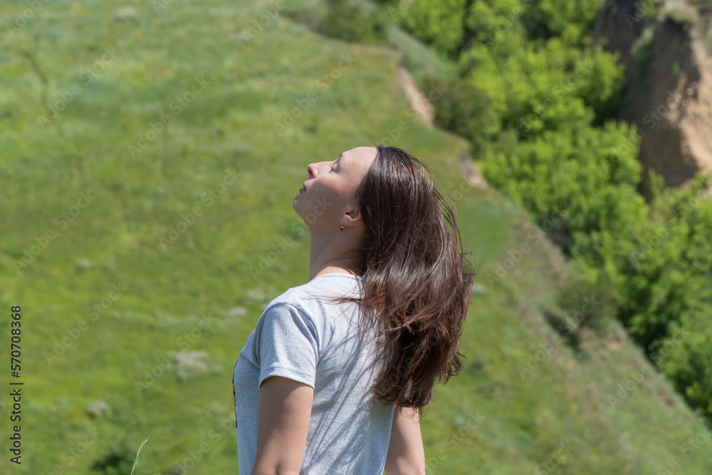 Portrait woman with long brown hair. Person posingin standing on ravine covered with greenery. Confident young adult female makes head movement and wind blowing hair. Enjoyment of life in 35-45 years. Portrait woman with long brown hair. Person posingin standing on ravine covered with greenery. Confident young adult female makes head movement and wind blowing hair. Enjoyment of life in 35-45 years.
