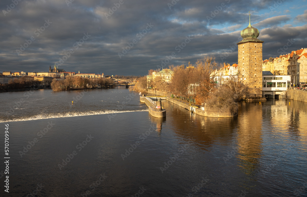 Fototapeta premium Winter evening with dark clouds and the setting sun by the river in the center of Prague