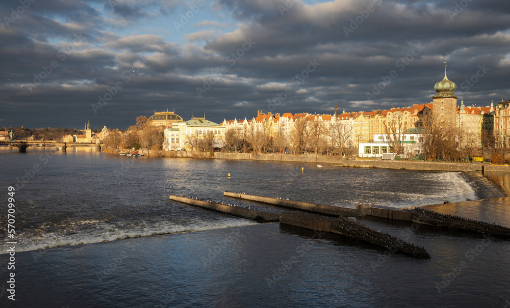 Obraz premium Winter evening with dark clouds and the setting sun by the river in the center of Prague