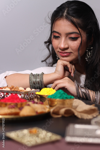 A woman girl lady in white dress with bangles arranging Abeer gulal dry color powder and Indian sweet Gujiya pedukiya kashew for the celebration of Holi festival of colors