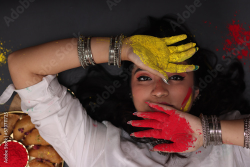 A beautiful woman girl lady laying down posing for the celebration of Holi festival of colors looking at the camera with Abeer gulal dry color powder and Indian sweet Gujiya pedukiya kashew photo