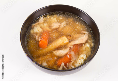 Chicken soup with noodle and carrot and parsley roots, chicken meat visible, in a bowl on a white background
