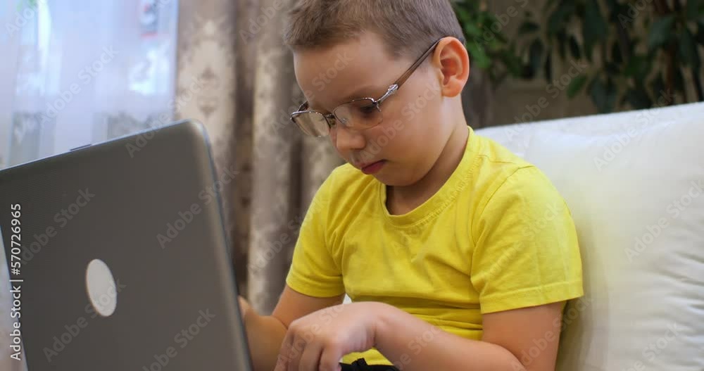 Child boy is typing on a laptop in glasses with a serious face and