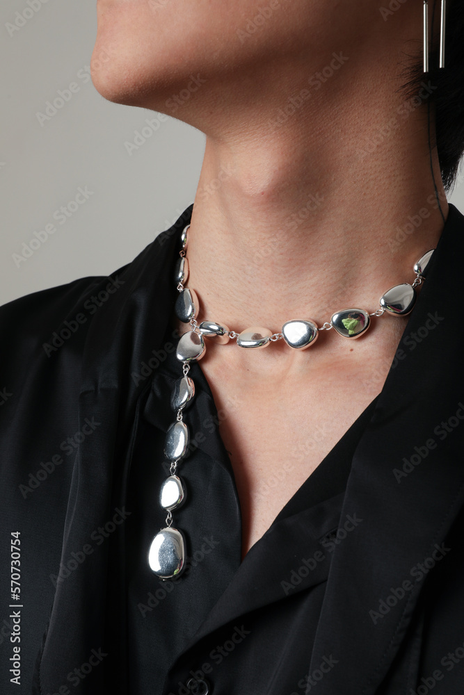 Close-up of young man wearing silver necklace posing indoor. Vertical mock-up.