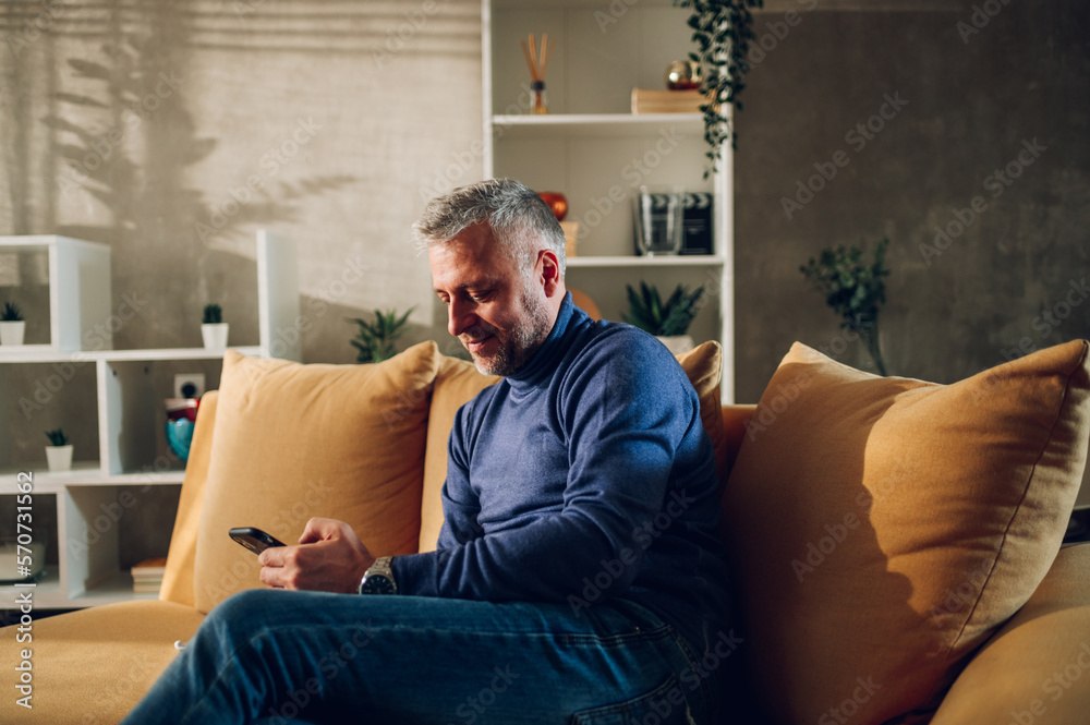 Middle aged man using smartphone while sitting on a sofa at home