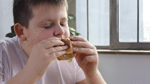 Little boy in fast food cafe eats burger. Portrait of hungry child Cute little kid eating burger. Hungry child in fast food cafe. Close-up boy eating burger. Hungry child in cafe. Lovely boy