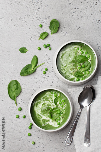 Two ceramic bowls with spinach cream soup with green pea and fresh spinach leaves on grey concrete background. Top view