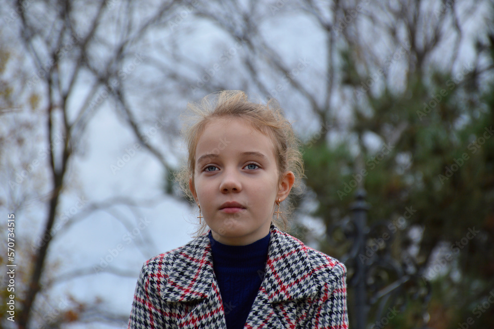 portrait of a beautiful girl in a plaid coat on the background of nature close-up. the child smiles a little and looks away. active lifestyle and outdoor activities portrait of a beautiful girl in a plaid coat on the background of nature close-up. the child smiles a little and looks away. active lifestyle and outdoor activities