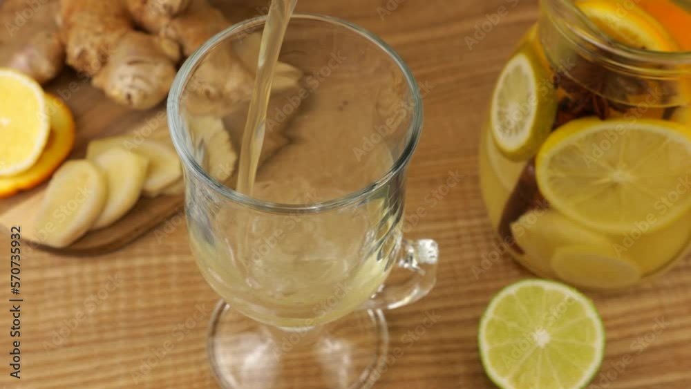 Cooking a drink of citrus and ginger to boost immunity. Lemonade is poured into a glass against the background of slices of orange, lemon, lime, ginger and a glass jug of lemonade. Cooking a drink of citrus and ginger to boost immunity. Lemonade is poured into a glass against the background of slices of orange, lemon, lime, ginger and a glass jug of lemonade.