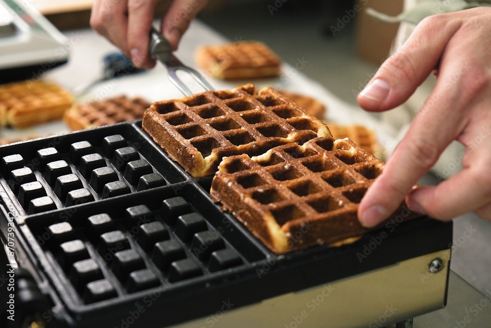 belgian waffles in a waffle iron. the cook pulls the finished Belgian