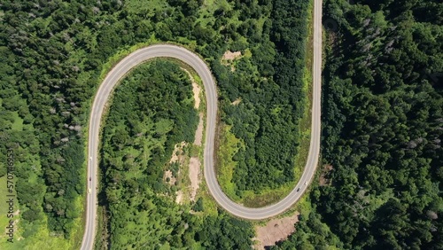 Aerial shot of a winding road passing through a dense green forest and car traveling to its destination