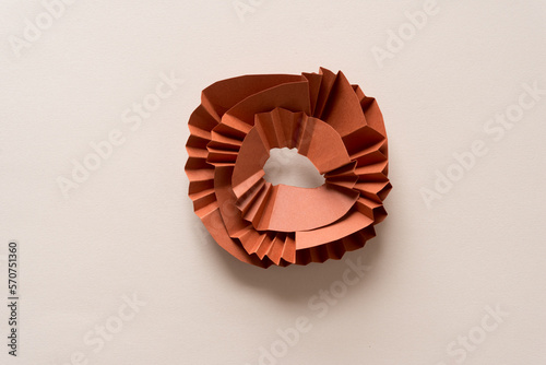 partly fan-folded or pleated brown paper circle-shapes on blank beige paper