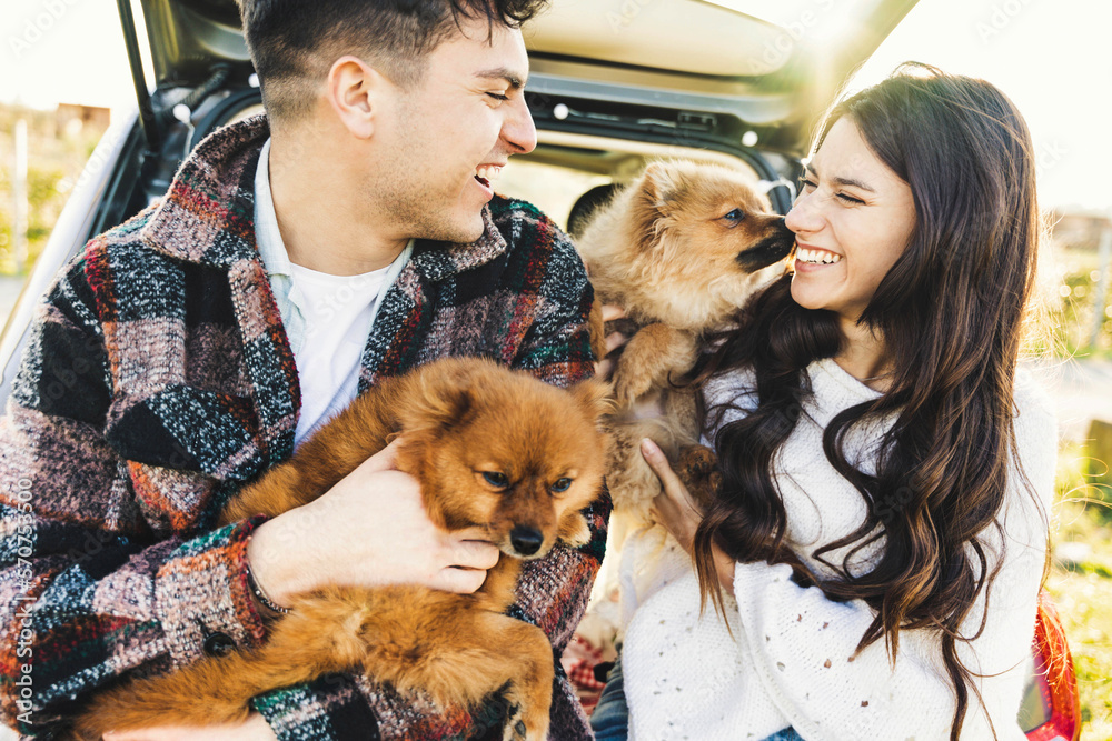 Happy couple sitting in the back of their car playing with dog - Romantic young family enjoying weekend roadtrip Happy couple sitting in the back of their car playing with dog - Romantic young family enjoying weekend roadtrip