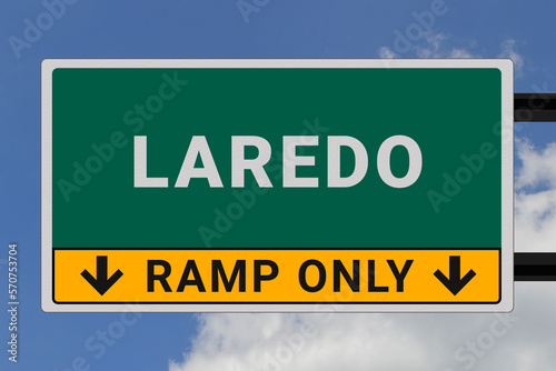 Laredo logo. Laredo lettering on a road sign. Signpost at entrance to Laredo, USA. Green pointer in American style. Road sign in the United States of America. Sky in background