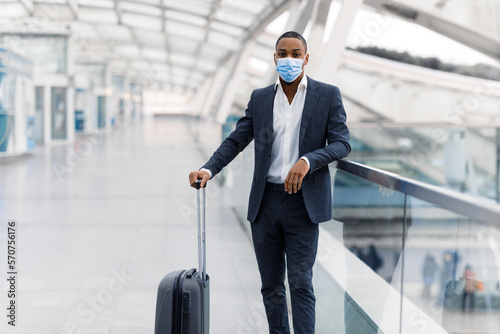 Black businessman wearing suit and medical mask standing on walkway at airport