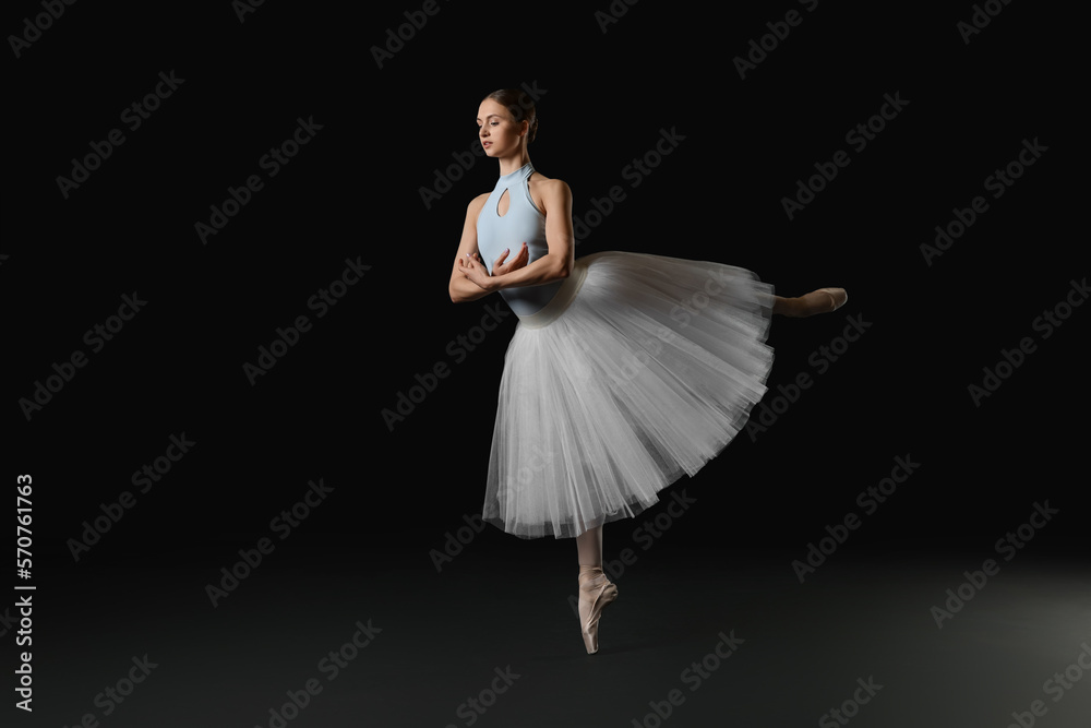 Fototapeta premium Young ballerina practicing dance moves on black background