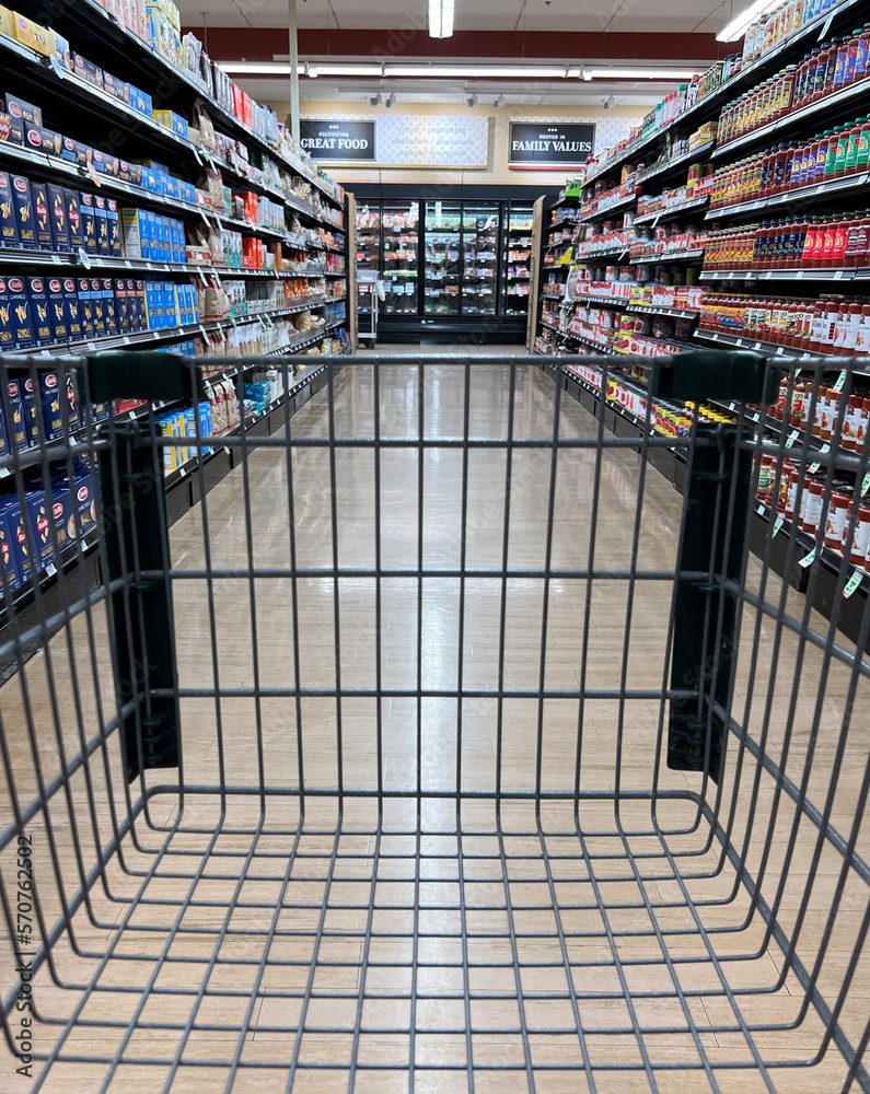 Looking down the aisle of a supermarket through a shopping cart.