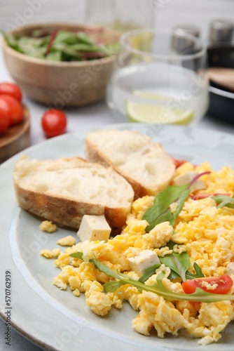 Plate with delicious scrambled eggs, tofu and slices of baguette on table, closeup