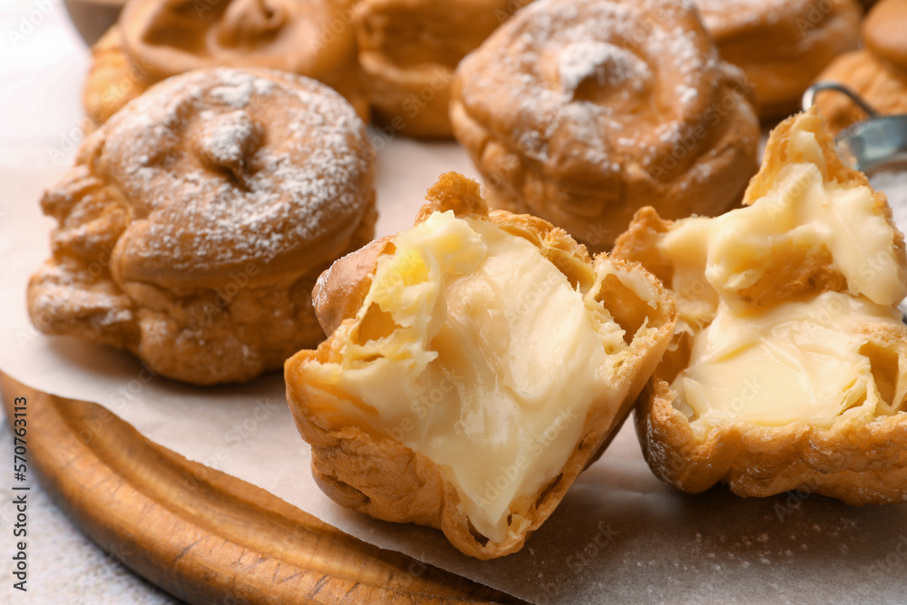 Delicious profiteroles filled with cream on wooden board, closeup
