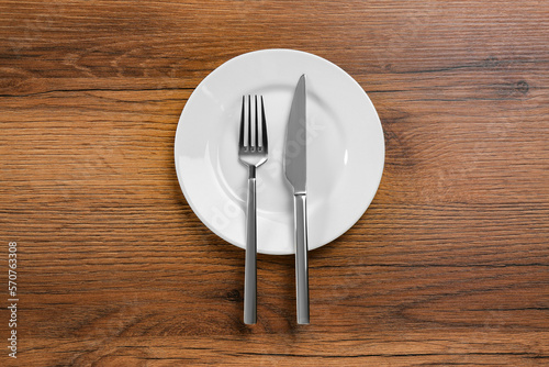 White plate  fork and knife on wooden table  top view
