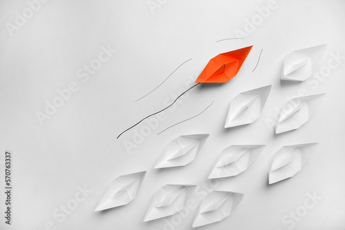 Fotografie Orange paper boat floating past others on white background, flat lay with space for text