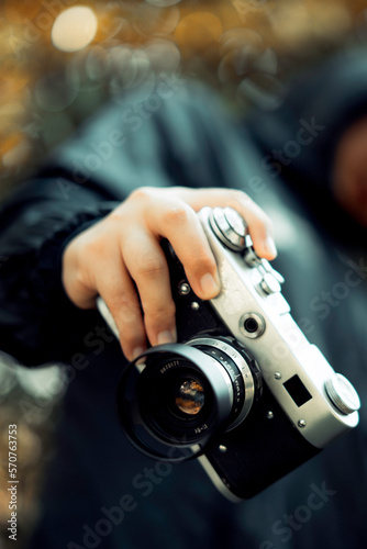 woman taking a picture with a camera, film camera in the hands of a girl taking a picture. Green trees bokeh background, woman taking a photo with a camera, selective focus, soft focus.