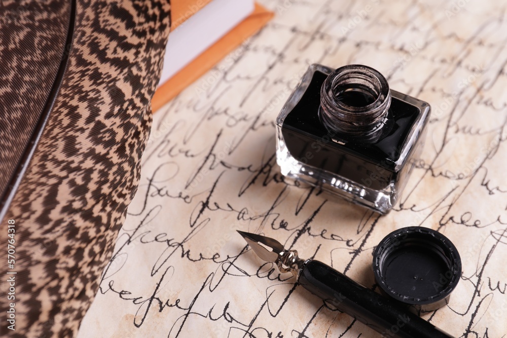 Open inkwell, fountain pen, feather and book on vintage parchment with text, closeup