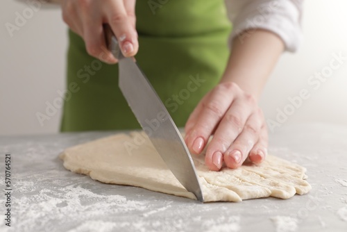 Woman cutting dough at light grey marble table, closeup. Cooking grissini