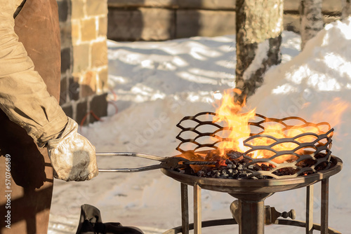 In the hand of a blacksmith, old tongs with an iron rod over burning coals in a blacksmith's forge.Hand craft outdoors in winter. photo