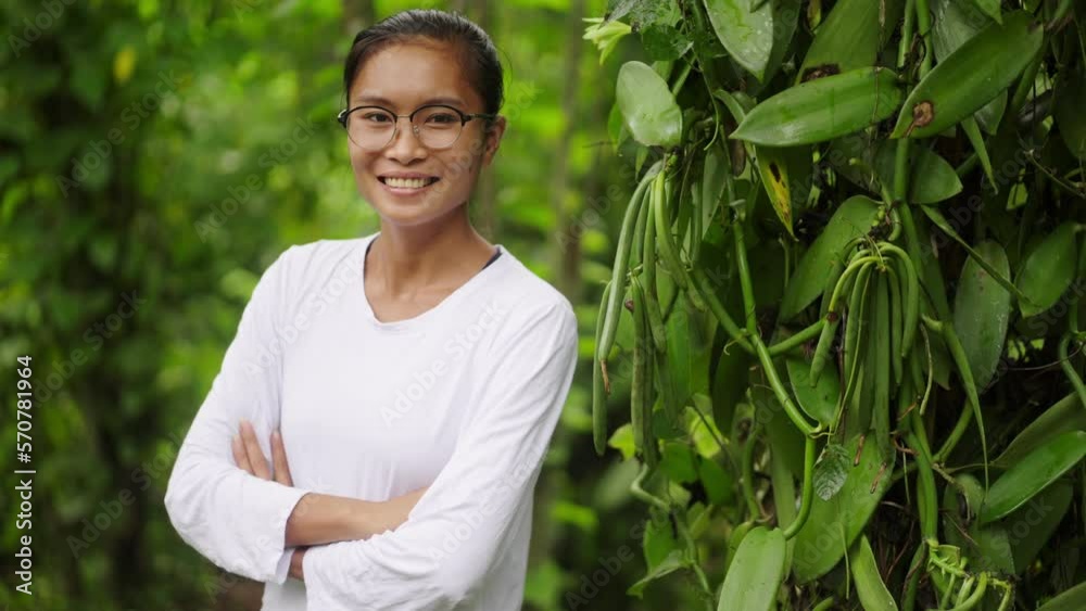 Beautiful portrait of female vanilla farmer standing arms crossed next to vanilla plant full of vanilla beans. Medium shot Beautiful portrait of female vanilla farmer standing arms crossed next to vanilla plant full of vanilla beans. Medium shot