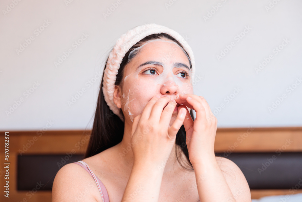 Caucasian girl on her bed, applying moisturizing facial sheet mask. Skin care at home. Caucasian girl on her bed, applying moisturizing facial sheet mask. Skin care at home.