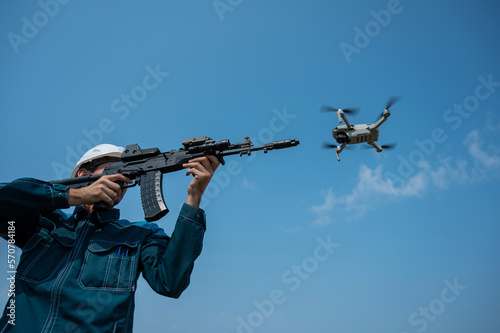 Caucasian man in a helmet shoots a flying drone with a rifle. 