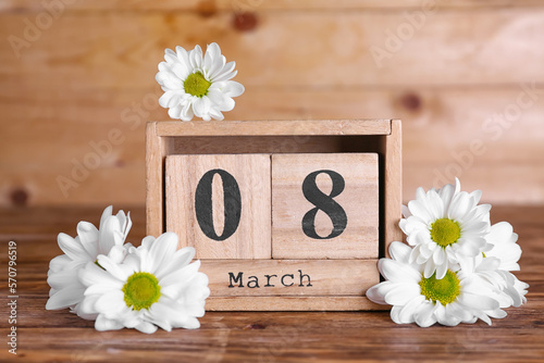 Cube calendar with date MARCH 8 and beautiful chamomile flowers on wooden table. Women's Day celebration