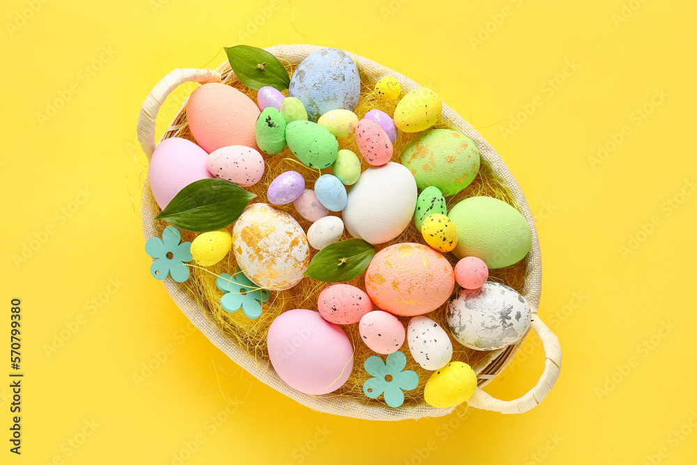 Fototapeta premium Basket with beautiful Easter eggs and plant leaves on yellow background