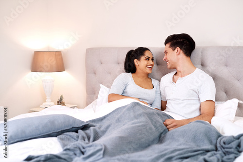 Bedroom, love and interracial couple laughing together in home holding hands at night. Smiling, diversity and marriage of an Indian woman and man with care and relax happiness with a smile in a house